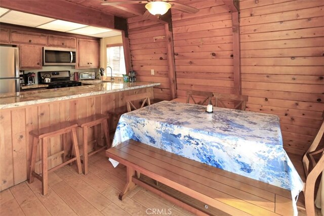 interior space with sink, wood walls, stainless steel refrigerator, ceiling fan, and light hardwood / wood-style flooring