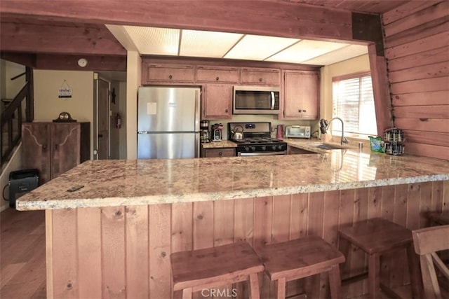 kitchen featuring wood walls, kitchen peninsula, sink, a kitchen breakfast bar, and stainless steel appliances