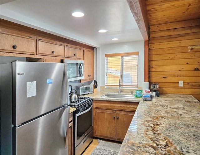 kitchen featuring brown cabinetry, light stone counters, stainless steel appliances, and a sink