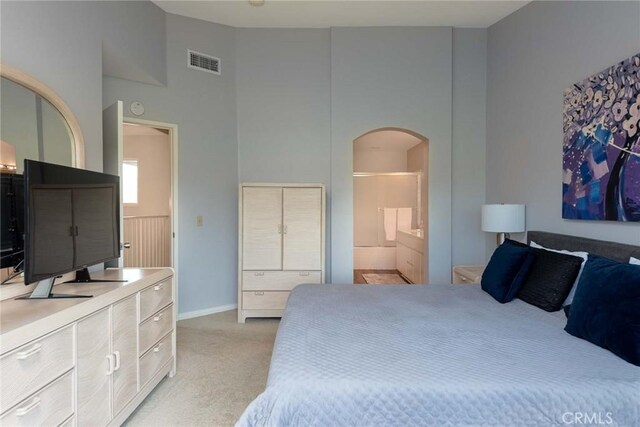 bedroom with light colored carpet, ensuite bathroom, and a towering ceiling