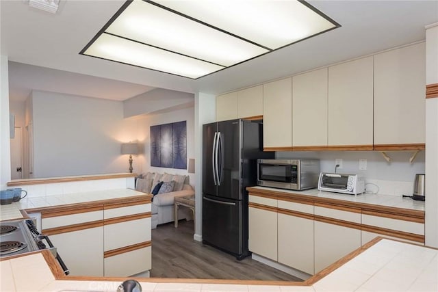 kitchen with tile counters, black refrigerator, wood-type flooring, and kitchen peninsula