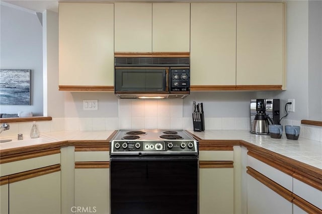 kitchen featuring tile counters, sink, electric range oven, and cream cabinets