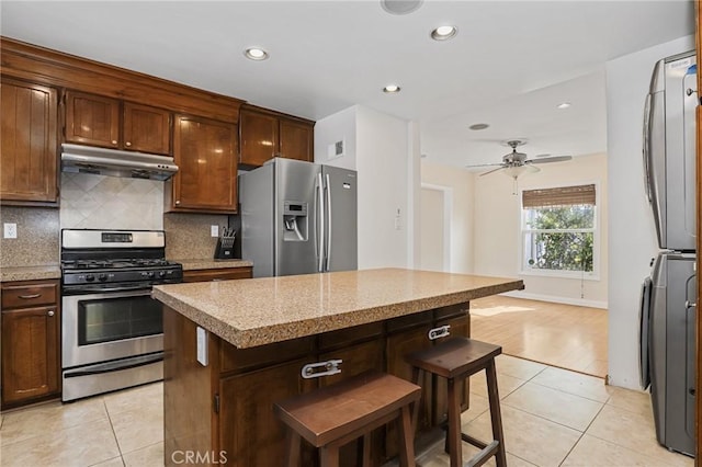 kitchen with light tile patterned floors, stacked washer and clothes dryer, ceiling fan, stainless steel appliances, and a center island