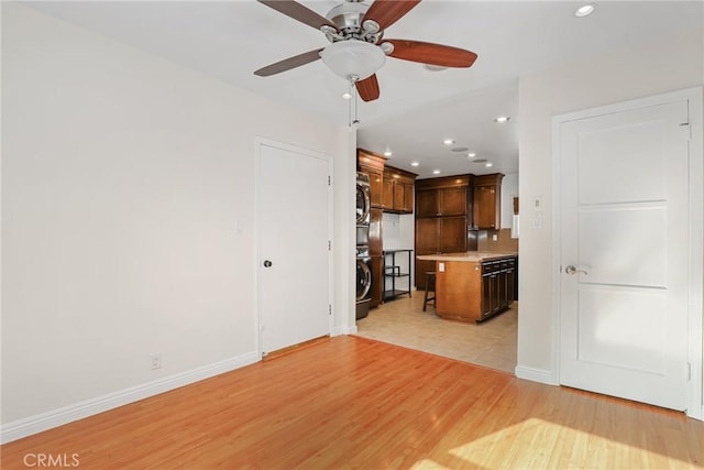 kitchen with ceiling fan, light hardwood / wood-style floors, a kitchen island, stacked washing maching and dryer, and white refrigerator