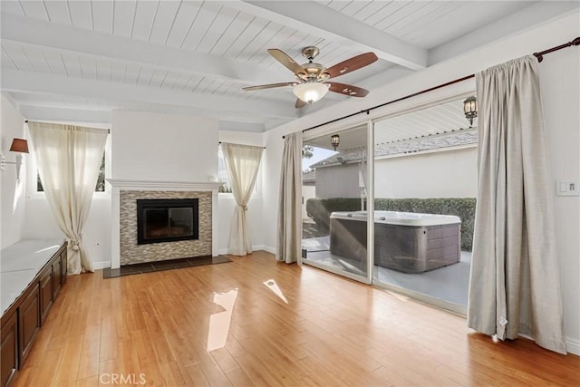 unfurnished living room featuring beam ceiling, ceiling fan, a fireplace, and light hardwood / wood-style flooring