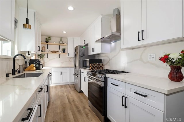 kitchen featuring wall chimney range hood, pendant lighting, sink, white cabinetry, and stainless steel appliances