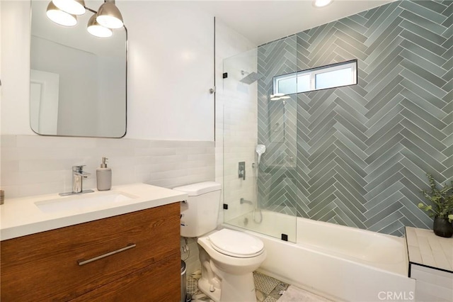 full bathroom featuring toilet, enclosed tub / shower combo, tile walls, and vanity