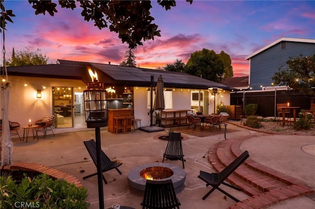 back house at dusk with a patio area, an outdoor fire pit, exterior bar, and solar panels