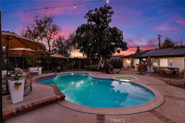 pool at dusk with an in ground hot tub and a patio