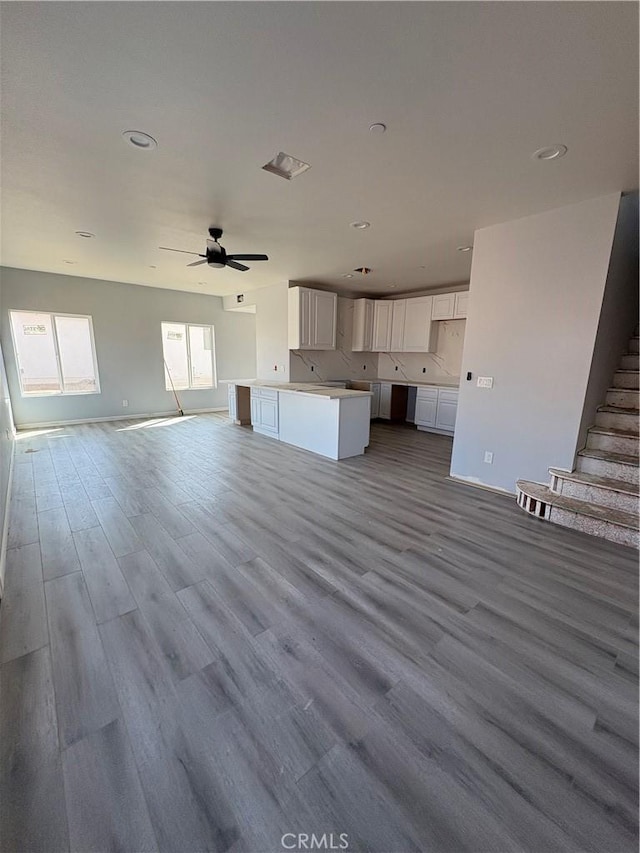 unfurnished living room featuring baseboards, stairs, ceiling fan, and wood finished floors