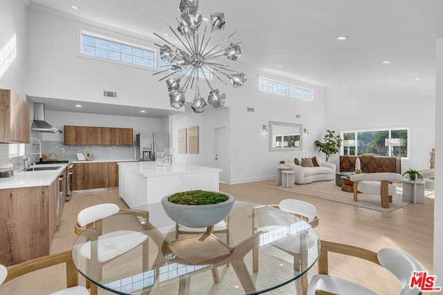 dining area with a towering ceiling, a chandelier, sink, and light wood-type flooring