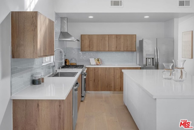 kitchen featuring wall chimney exhaust hood, sink, tasteful backsplash, light hardwood / wood-style flooring, and appliances with stainless steel finishes