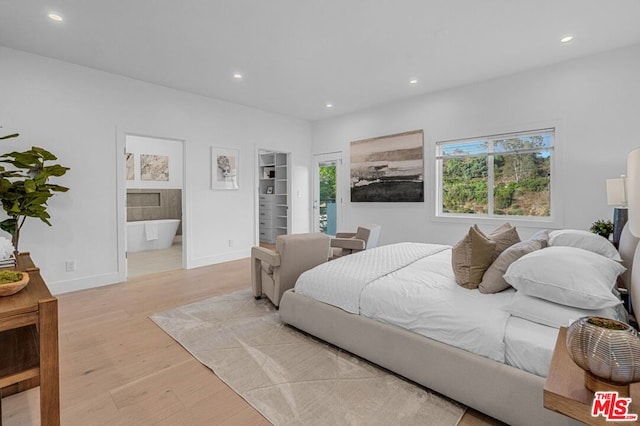 bedroom featuring a walk in closet, light wood-type flooring, and ensuite bathroom