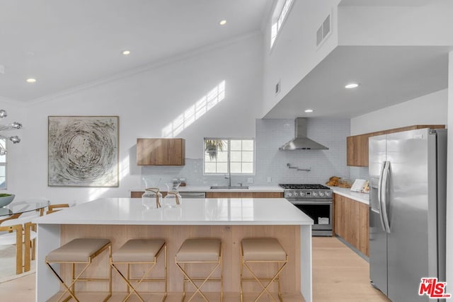 kitchen with wall chimney exhaust hood, appliances with stainless steel finishes, a kitchen bar, and sink