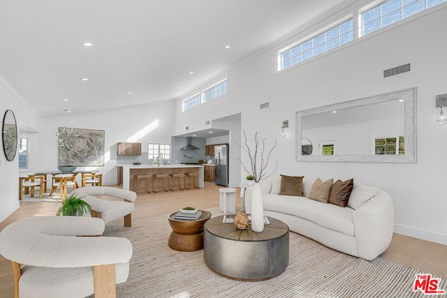 living room featuring sink, crown molding, light hardwood / wood-style floors, and a towering ceiling