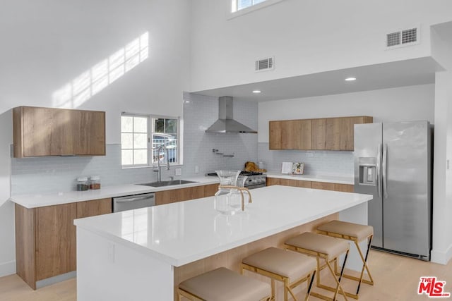 kitchen featuring appliances with stainless steel finishes, wall chimney exhaust hood, a kitchen breakfast bar, and a kitchen island with sink