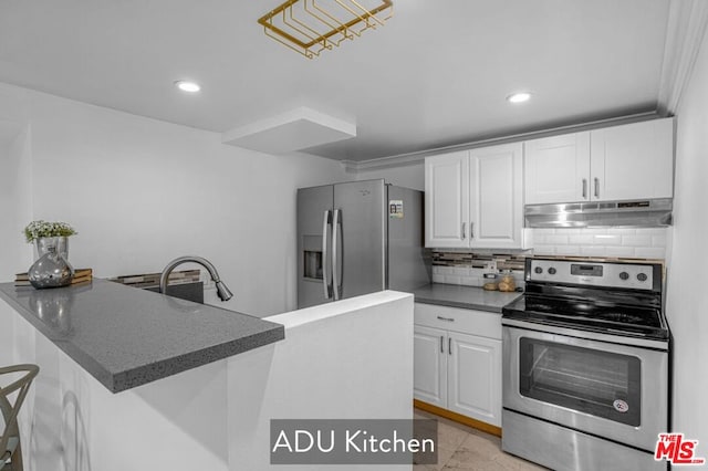 kitchen with appliances with stainless steel finishes, backsplash, white cabinets, a kitchen breakfast bar, and kitchen peninsula