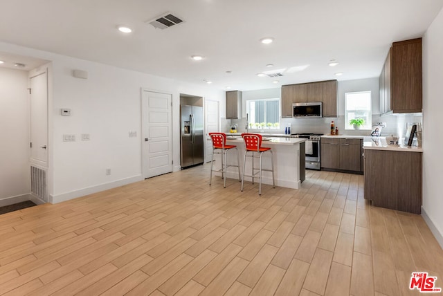 kitchen featuring backsplash, a center island, a breakfast bar, light wood-type flooring, and stainless steel appliances