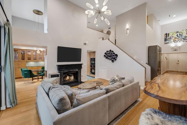 living room featuring an inviting chandelier, a fireplace, light wood-type flooring, and a high ceiling