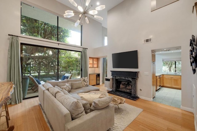 living room with a high ceiling, a notable chandelier, a high end fireplace, a healthy amount of sunlight, and light wood-type flooring