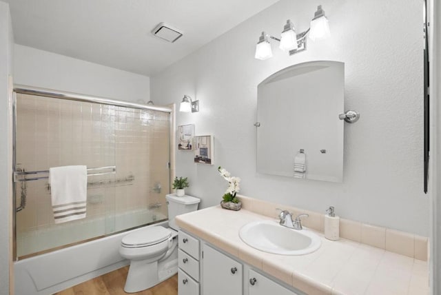 full bathroom with vanity, hardwood / wood-style floors, shower / bath combination with glass door, and toilet