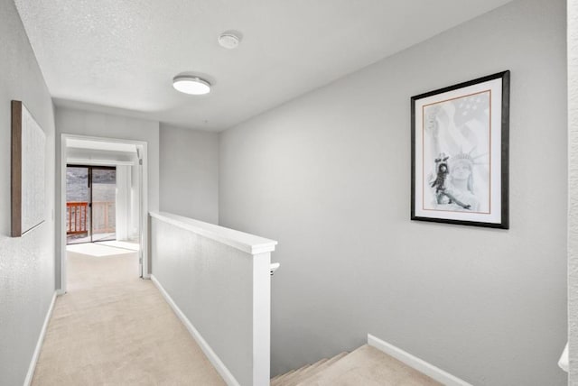 corridor with light colored carpet and a textured ceiling