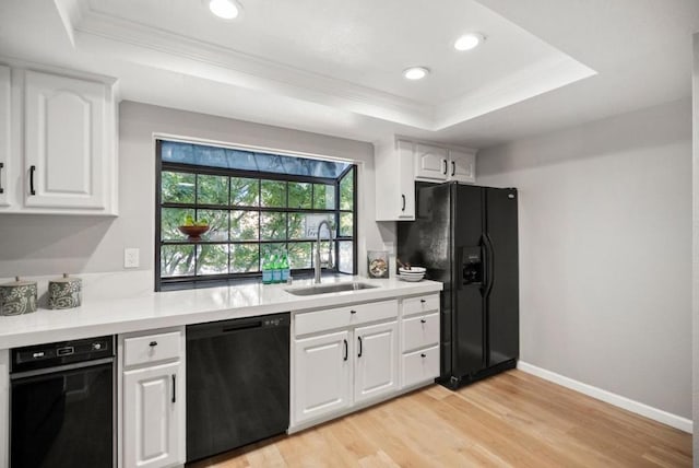 kitchen featuring black appliances, white cabinetry, sink, a tray ceiling, and light wood-type flooring