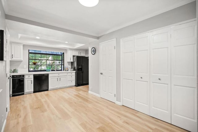 kitchen featuring white cabinetry, ornamental molding, black appliances, a raised ceiling, and light wood-type flooring