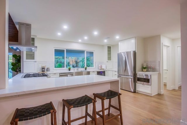 kitchen with extractor fan, kitchen peninsula, decorative backsplash, white cabinetry, and stainless steel appliances