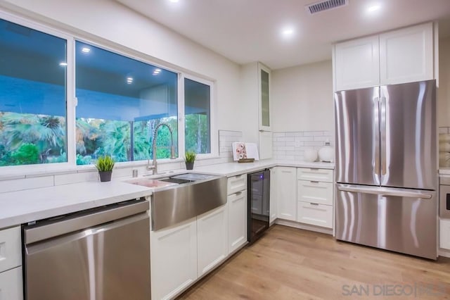 kitchen featuring backsplash, sink, light wood-type flooring, stainless steel appliances, and white cabinets