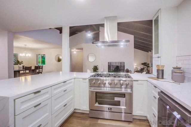 kitchen featuring kitchen peninsula, stainless steel range, a notable chandelier, wall chimney range hood, and white cabinets