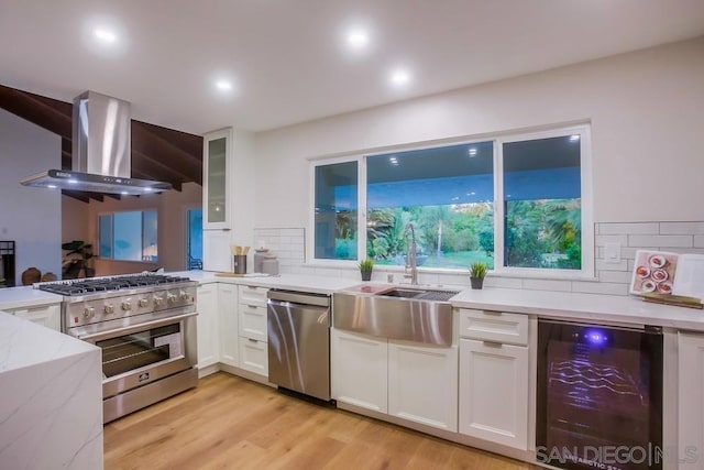 kitchen with stainless steel appliances, beverage cooler, wall chimney range hood, white cabinets, and sink