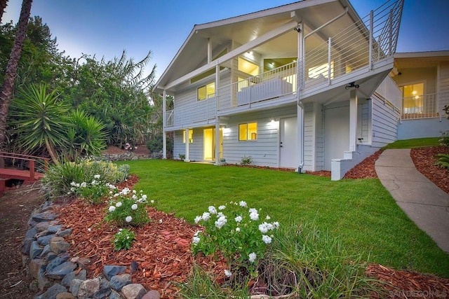 back house at dusk featuring a yard and a balcony