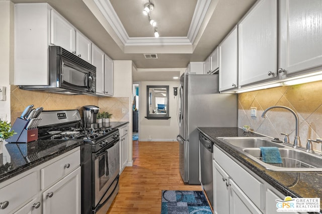 kitchen with white cabinets, stainless steel appliances, sink, a raised ceiling, and light wood-type flooring