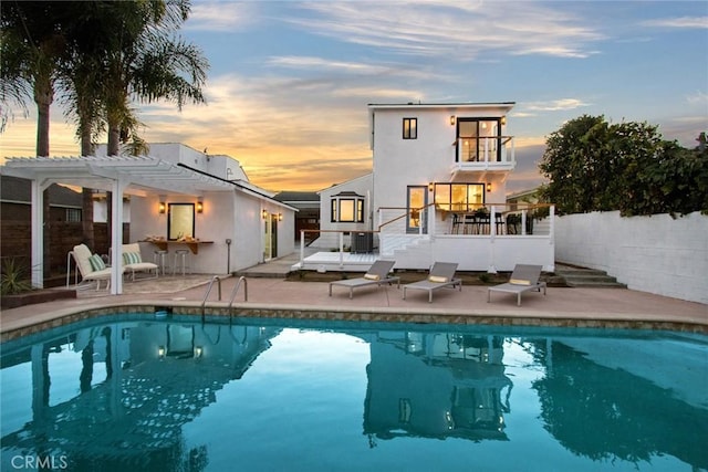 back house at dusk featuring central AC unit, a pergola, a pool side deck, and a patio