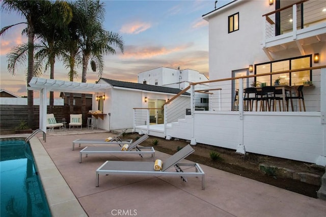 patio terrace at dusk with a fenced in pool and a pergola