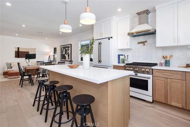 kitchen with white cabinets, a kitchen island, wall chimney range hood, tasteful backsplash, and high end appliances