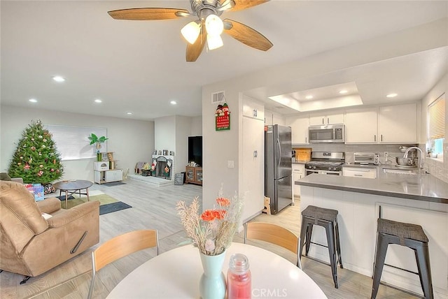 living room with ceiling fan, a raised ceiling, sink, and light hardwood / wood-style flooring