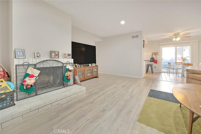 living room with ceiling fan, light hardwood / wood-style flooring, and a brick fireplace