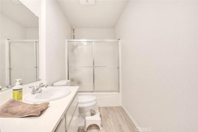 full bathroom featuring hardwood / wood-style floors, combined bath / shower with glass door, vanity, and toilet