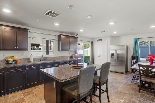 kitchen with visible vents, a kitchen island, appliances with stainless steel finishes, dark stone countertops, and a sink