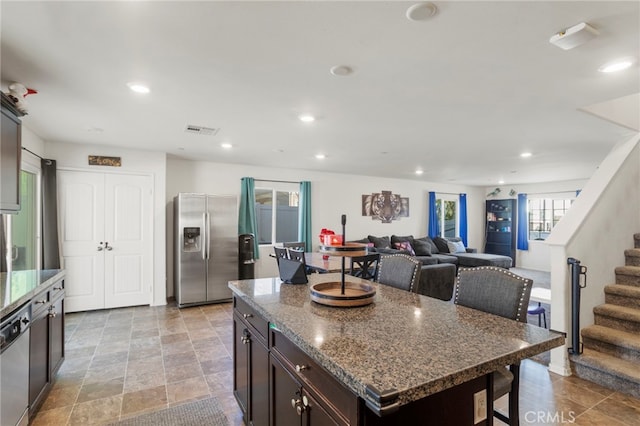 kitchen featuring appliances with stainless steel finishes, open floor plan, a kitchen island, dark stone countertops, and dark brown cabinets