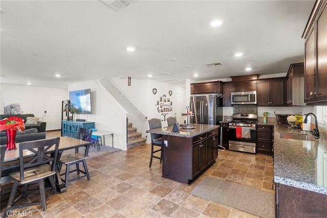 kitchen featuring stainless steel appliances, decorative backsplash, a center island, stone countertops, and sink