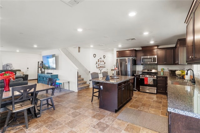 kitchen with stone countertops, appliances with stainless steel finishes, open floor plan, a center island, and a sink