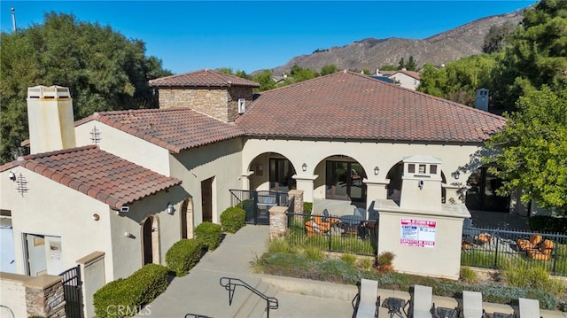 view of front of property featuring a mountain view, fence, a tiled roof, stone siding, and stucco siding