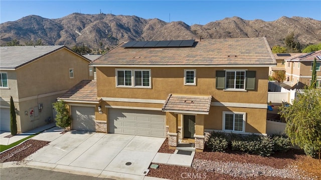 view of front facade with roof mounted solar panels, a mountain view, concrete driveway, and stucco siding