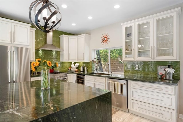 kitchen with wine cooler, wall chimney range hood, dark stone countertops, sink, and stainless steel appliances