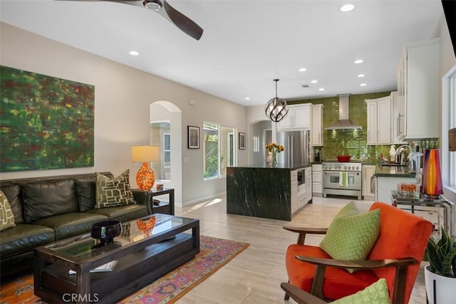 living room with light wood-type flooring, ceiling fan with notable chandelier, and sink