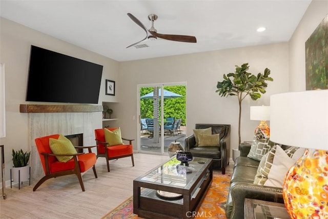 living room featuring ceiling fan, a tile fireplace, and light hardwood / wood-style flooring