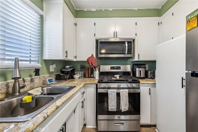 kitchen featuring white cabinets, appliances with stainless steel finishes, sink, and light stone counters